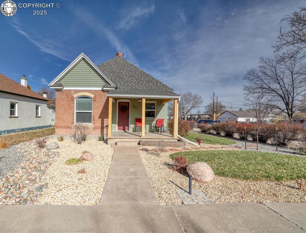 Caption: Traditional-style home featuring covered porch, roof with shingles, brick siding, a front yard