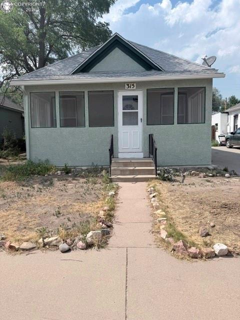 Caption: Light green stucco exterior with a dark green gable accent, featuring a screened-in porch, white fro
