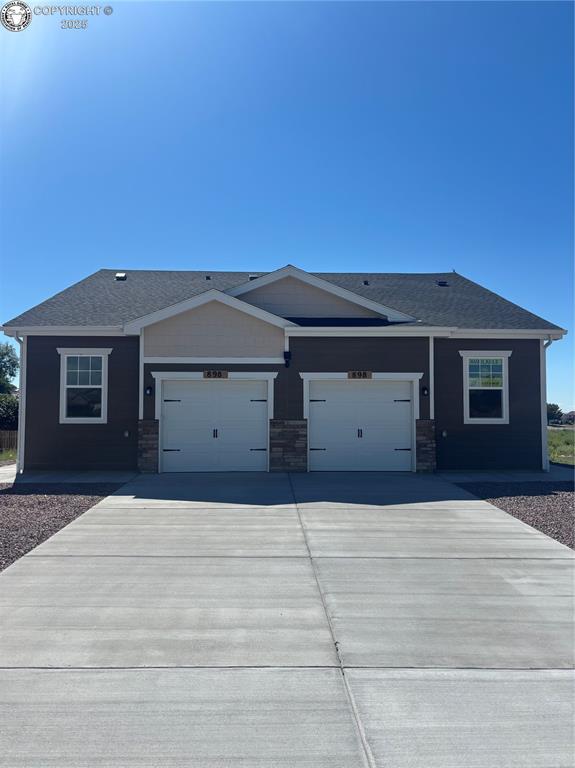 Caption: View of front of home with driveway, stone siding, and an attached garage