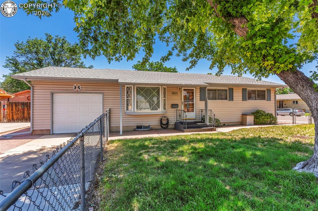 Caption: Ranch-style exterior with beige siding, a single-car garage, and a chain-link fence
