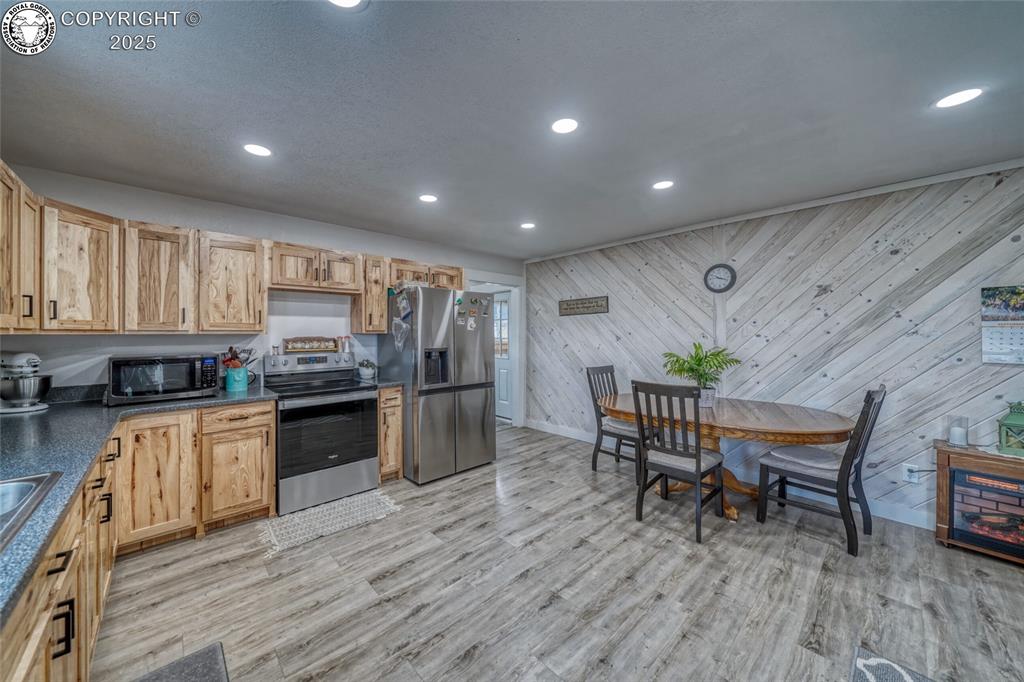 Caption: Kitchen with stainless steel appliances, wood walls, dark countertops, recessed lighting, and light 