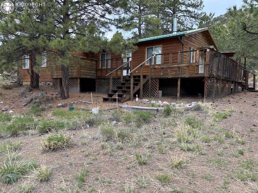 Caption: Rear view of house featuring stairs, a wooden deck, and log veneer siding