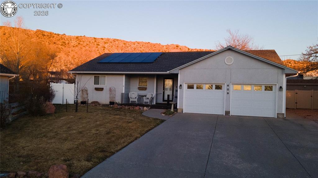 Caption: Ranch-style home with a gate, a porch, roof mounted solar panels, an attached garage, and concrete d