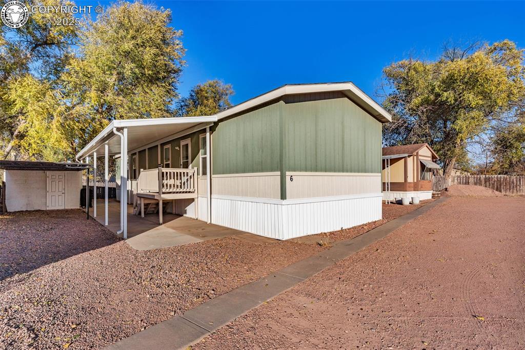 Caption: Front view with side entrance, big covered patio, carport, and secondary storage shed.