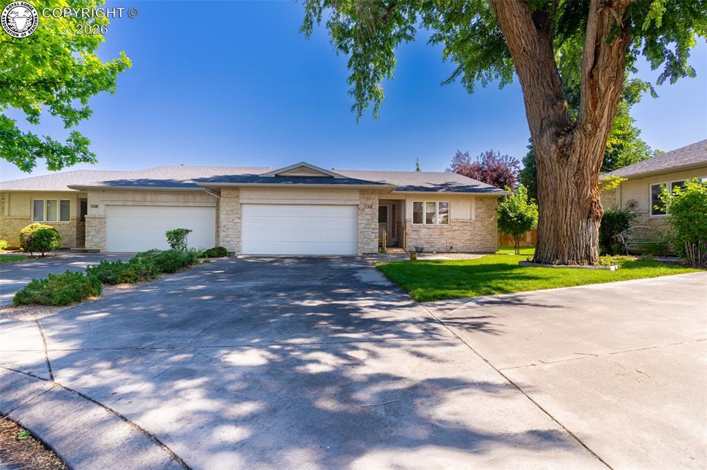 Caption: Stone facade home with a two-car garage, concrete driveway, and mature landscaping