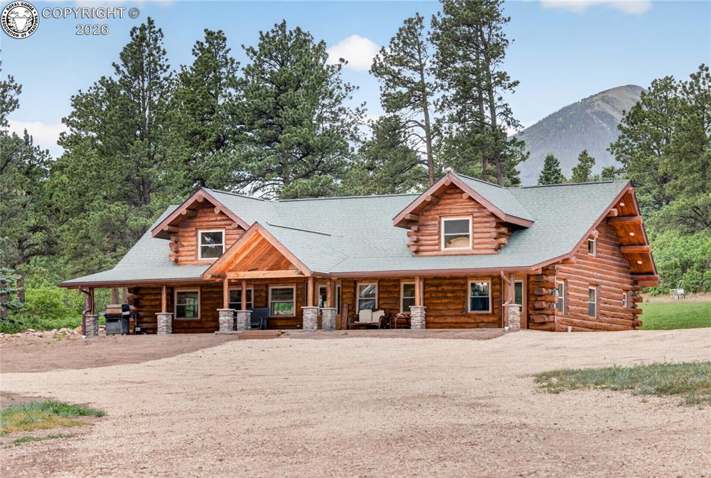 Caption: Log cabin style home featuring a covered front porch, dormer windows, natural wood siding, and a shi
