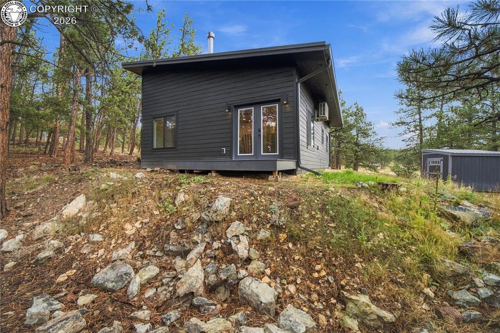 Caption: Modern exterior with dark horizontal siding, white-framed French doors, and a sloped roof