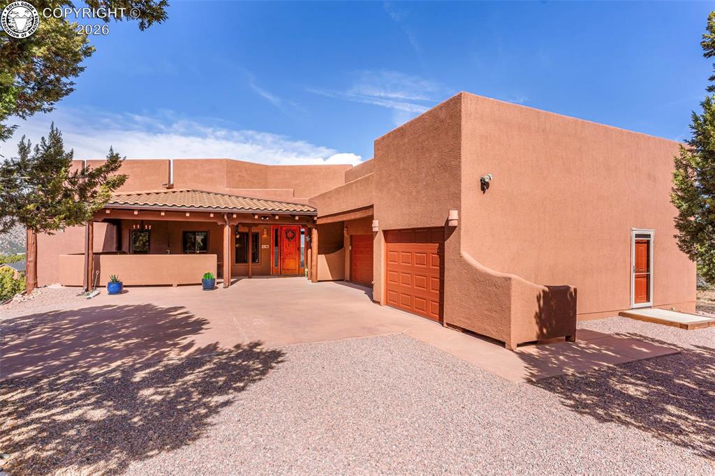 Caption: Pueblo-style exterior featuring a stucco facade, covered porch with exposed timber beams, tile roof 