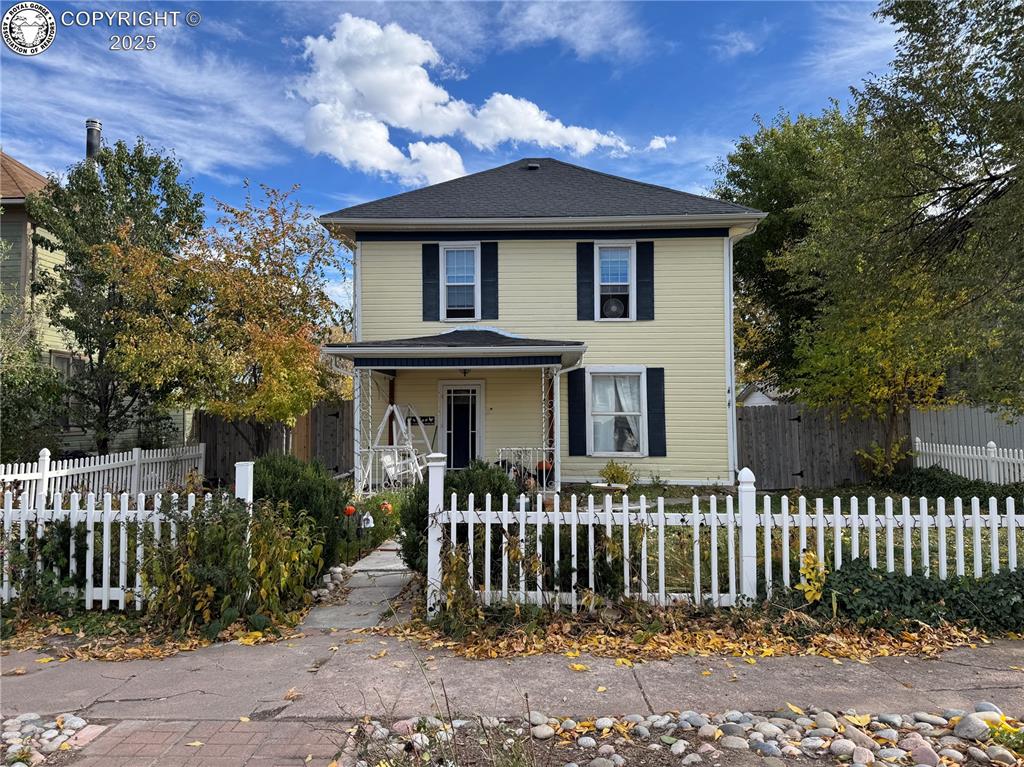 Caption: View of front of house with covered porch and a fenced front yard