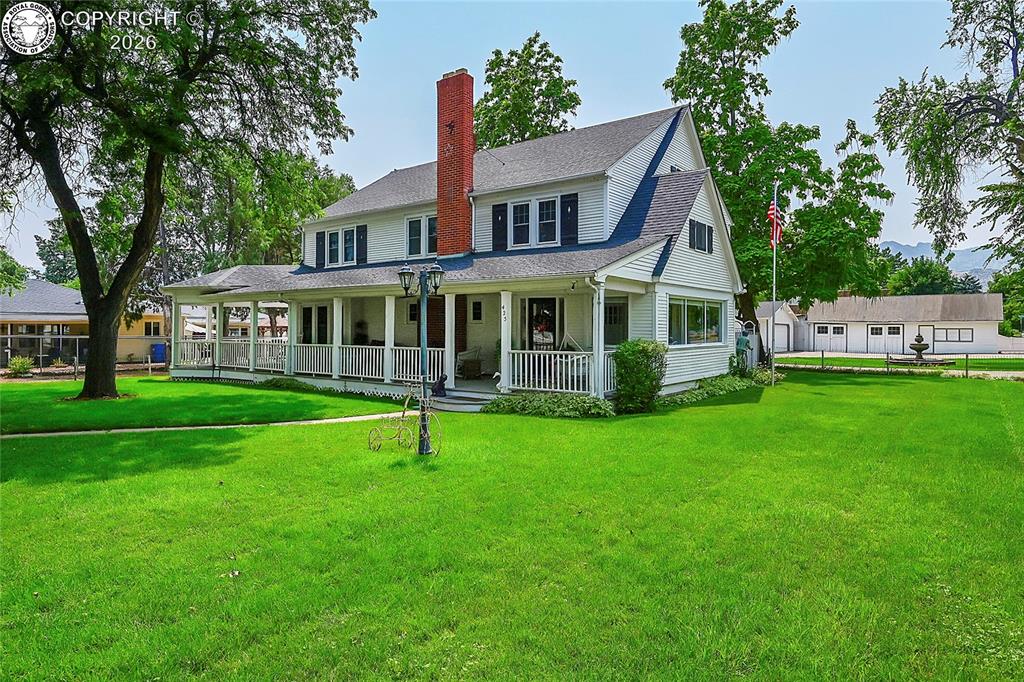 Caption: Rear view of property with a porch, a yard, a shingled roof, and a chimney