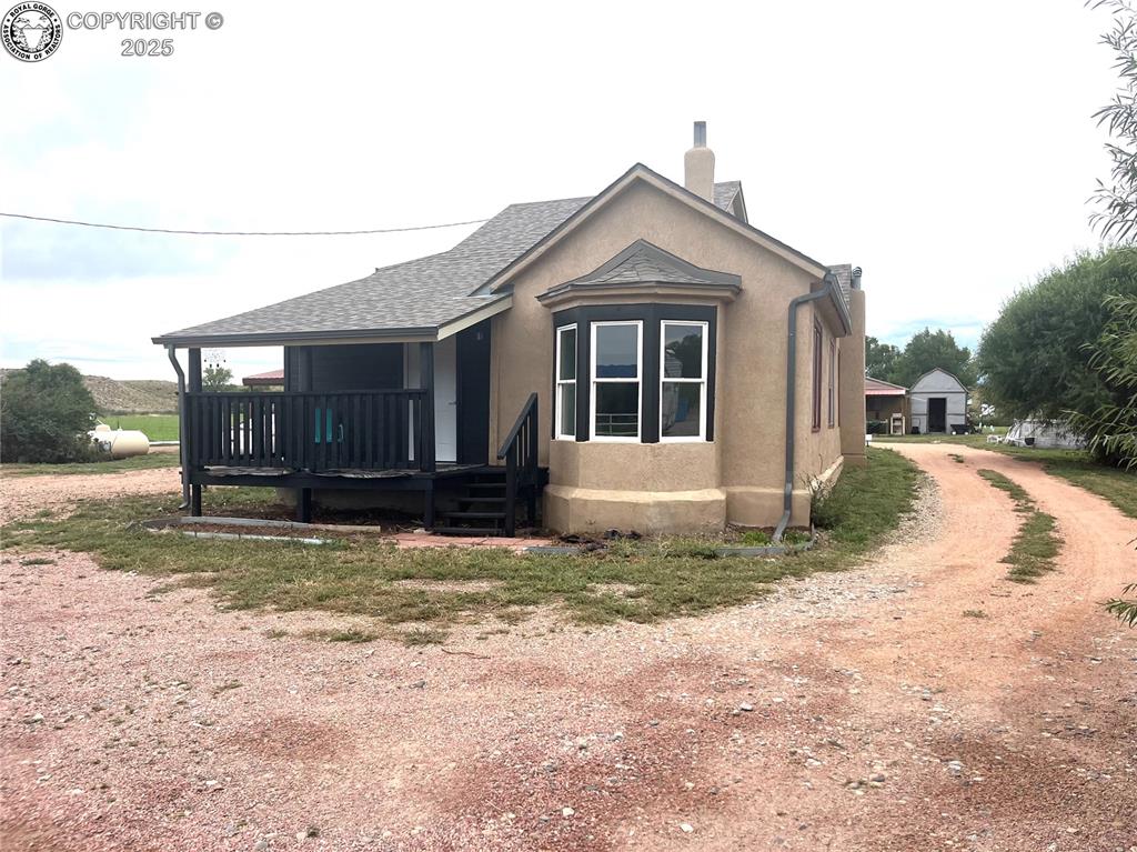 Caption: View of side of property featuring a chimney, stucco siding, and a shingled roof