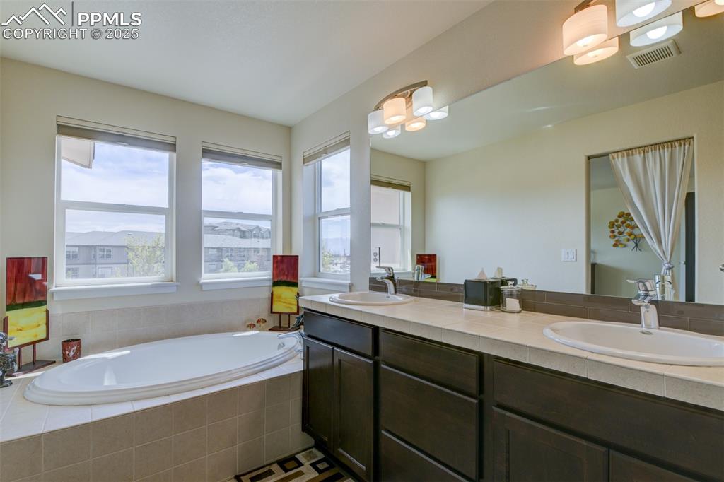 Image 28 of 45: Beautifully tiled primary bath with soaking tub, shower, dual vanity adjoin