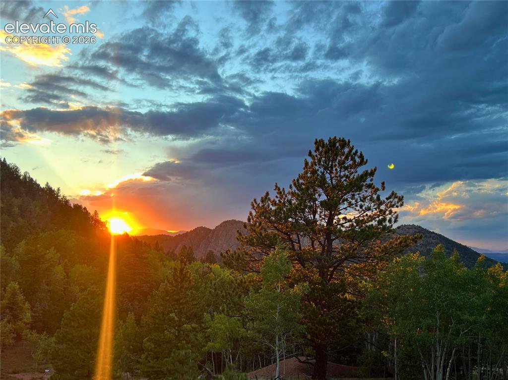 Image 38 of 46: Mountainous scenery with dense tree coverage and a prominent sunset