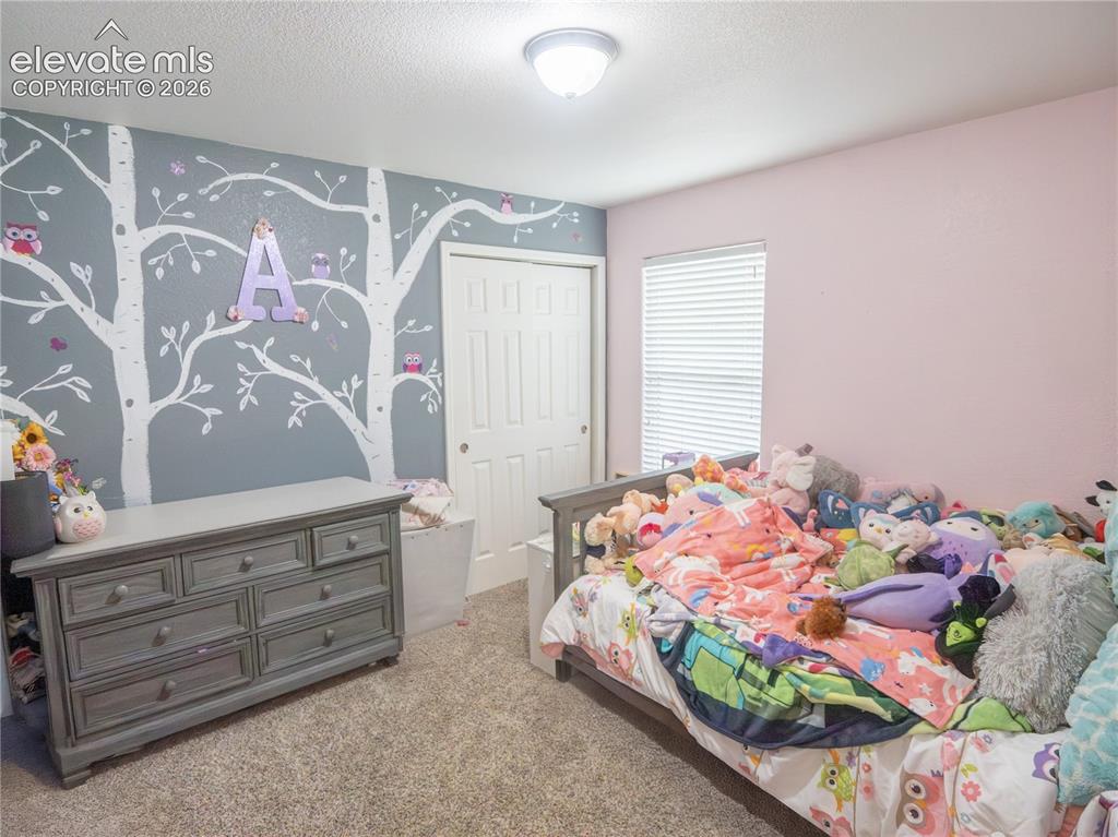 Image 9 of 13: Carpeted bedroom featuring a patterned accent wall and a window with blinds