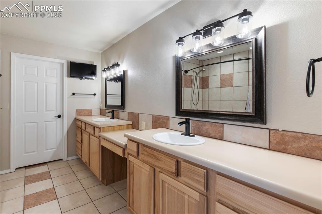 Image 24 of 29: Bathroom featuring dual vanities with light wood cabinetry and integrated s
