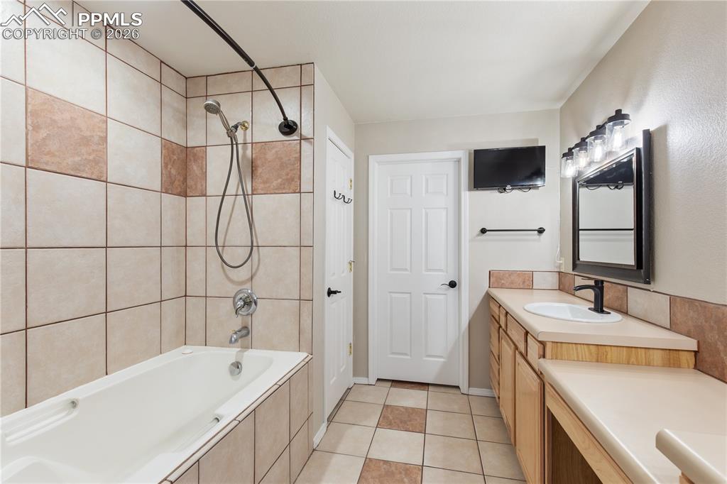 Image 26 of 29: Bathroom featuring a tiled tub surround with a handheld showerhead, a singl