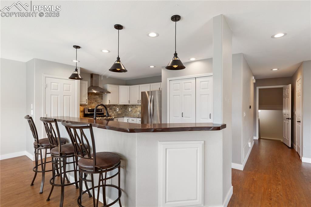 Image 7 of 29: Kitchen featuring a breakfast bar with a wood-finish countertop, white cabi
