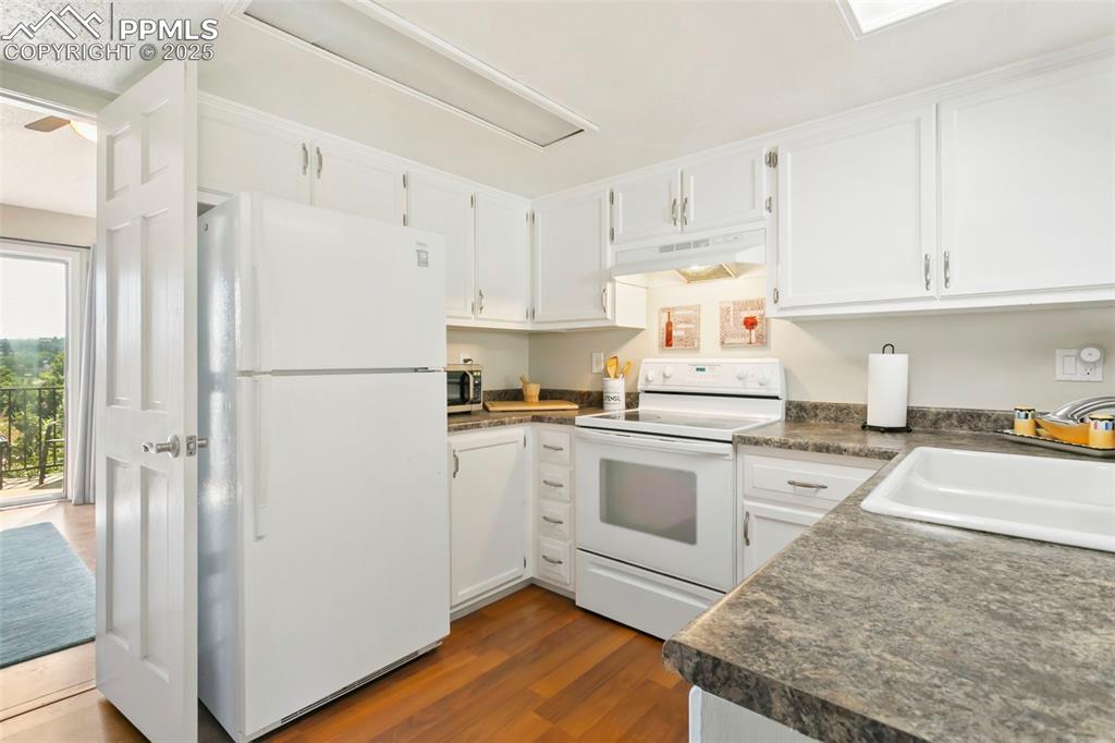 Image 5 of 17: Kitchen with dark countertops, white appliances, white cabinets, dark wood-