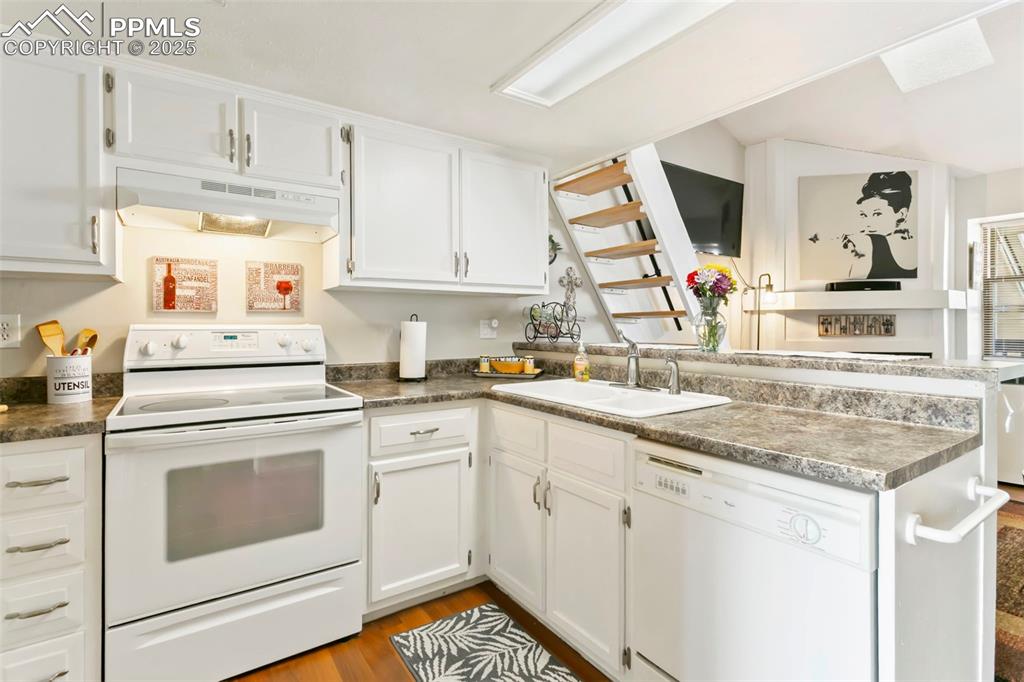 Image 7 of 17: Kitchen with white appliances, white cabinetry, a peninsula, and under cabi