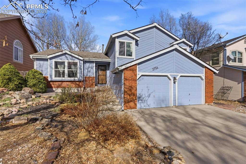 Caption: Tri-level home featuring concrete driveway, brick siding, and an attached garage