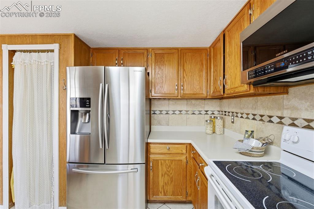 Image 12 of 45: Kitchen with stainless steel appliances, light countertops, wood finish cab