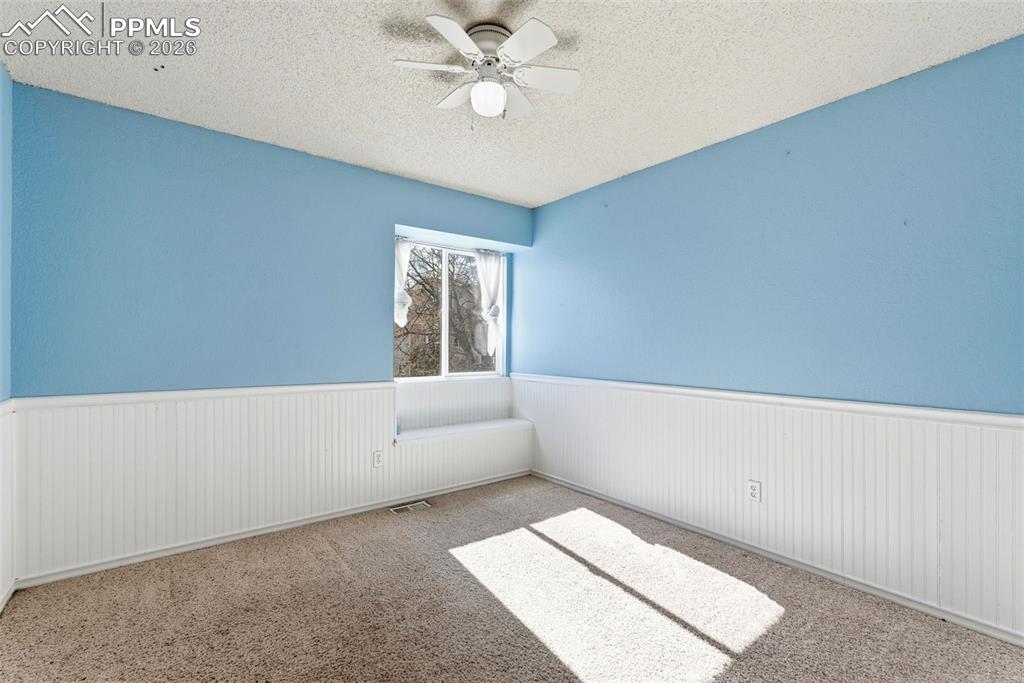 Image 25 of 45: Spare room featuring a textured ceiling, ceiling fan, a wainscoted wall, an