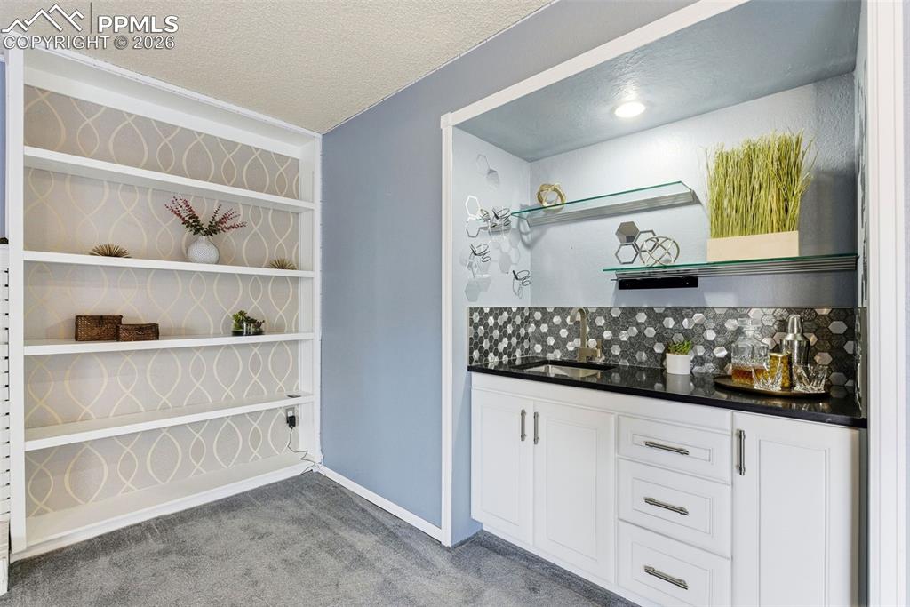 Image 31 of 45: Bar with open shelves, white cabinetry, light carpet, a textured ceiling, a