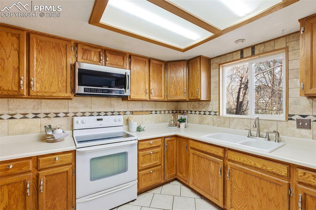 Image 8 of 45: Kitchen with white electric range, wood finish cabinetry, stainless steel m