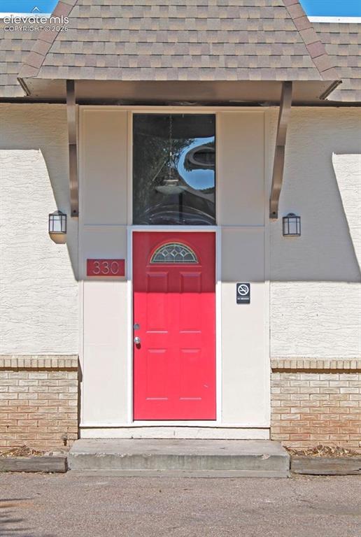Image 2 of 12: Red front door with an arched window insert, two exterior wall sconces, and