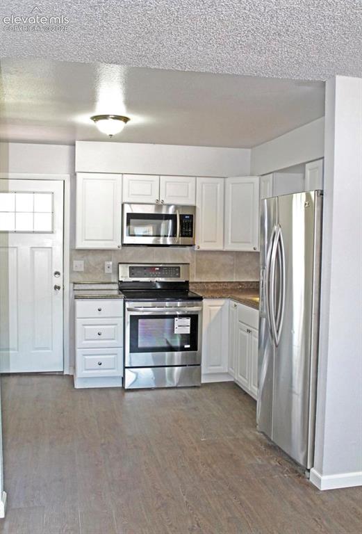 Image 4 of 12: Kitchen featuring wood-finish flooring, white cabinetry, stainless steel ap