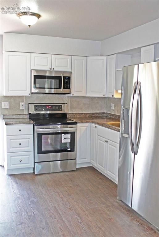 Image 6 of 12: White cabinetry, stainless steel appliances, wood-finish flooring, and a ti
