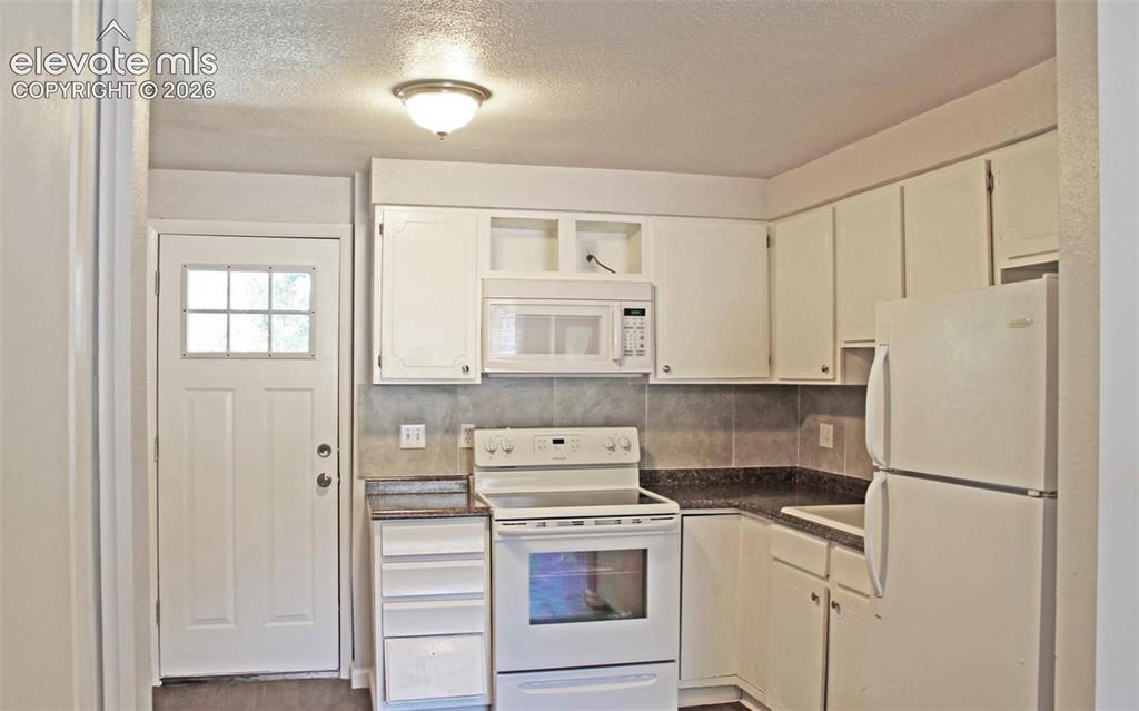 Image 8 of 12: White cabinetry, white appliances, dark countertops, tiled backsplash, and 
