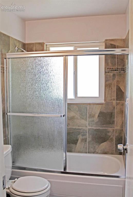 Image 9 of 12: Bathtub with a sliding glass shower enclosure, full wall tiling, and an int