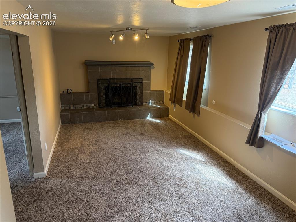 Image 12 of 17: Carpeted living space featuring a tile fireplace with decorative mosaic acc