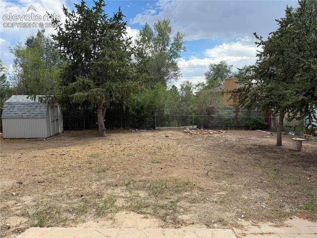Image 16 of 17: Expansive backyard featuring mature trees, a storage shed with a shingled r