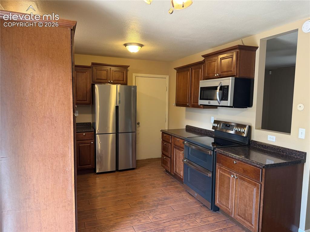 Image 5 of 17: Kitchen featuring wood-finish flooring, dark wood cabinetry, stainless stee