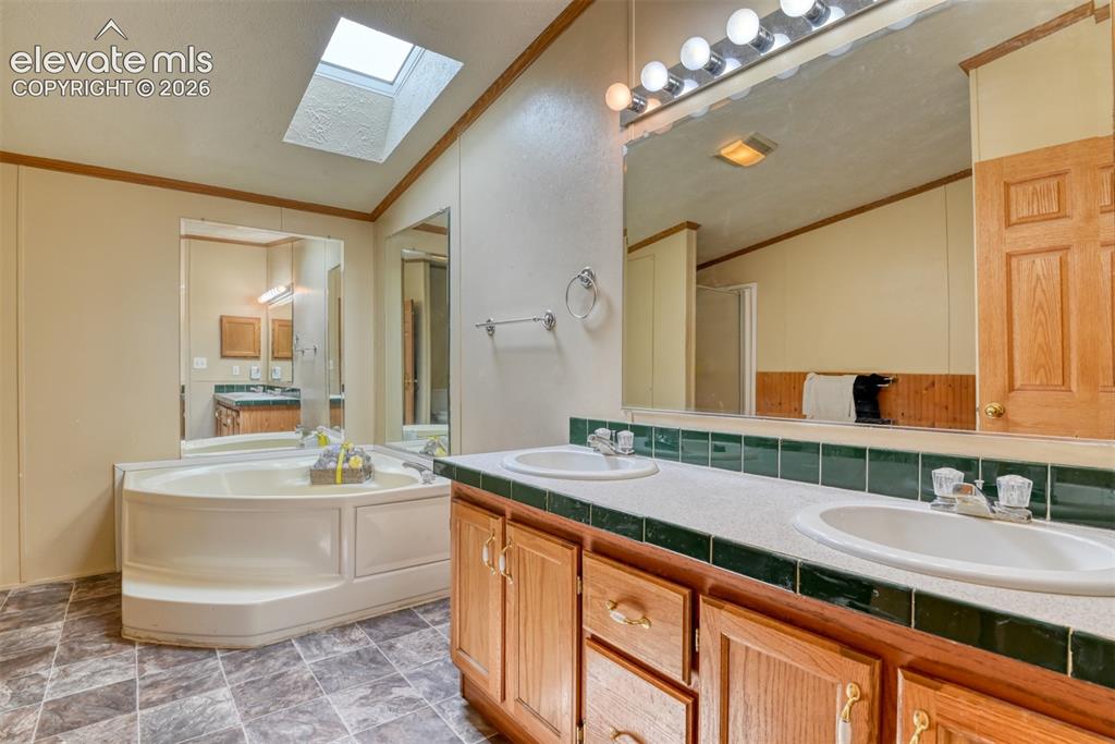 Image 20 of 37: Bathroom featuring a large soaking tub, skylight, dual vanities with integr