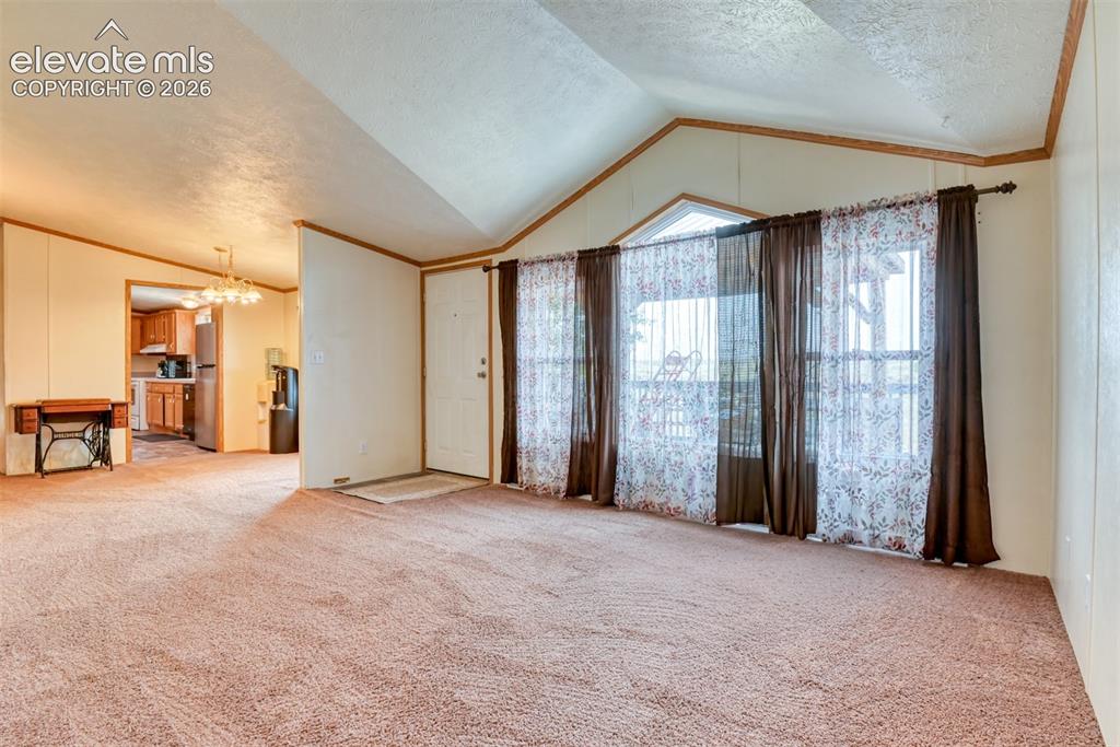 Image 30 of 37: Carpeted living area featuring vaulted ceilings and a front entry door with