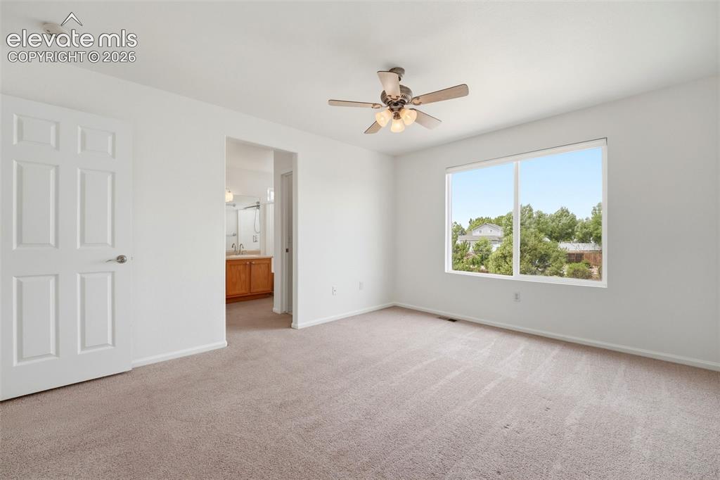 Image 21 of 48: Spacious room featuring neutral carpeting, a large window, and a ceiling fa
