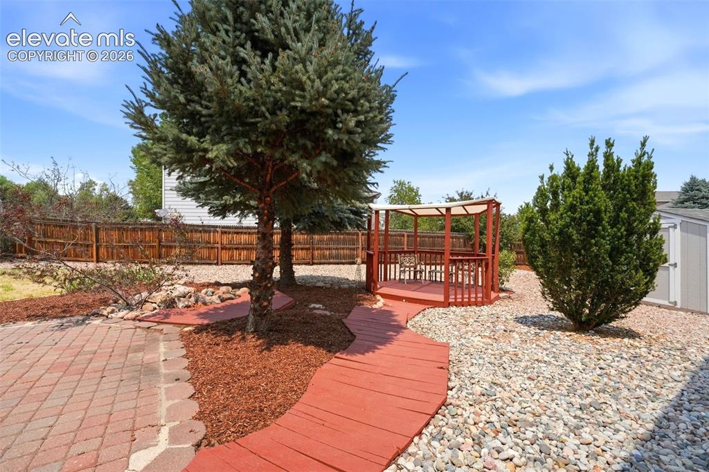 Image 34 of 48: Backyard featuring a red-stained wooden pathway, a raised pergola, and a pa