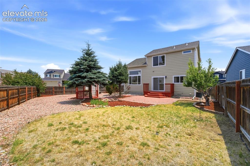 Image 35 of 48: Spacious backyard featuring a tan exterior home with a red-stained deck, ma