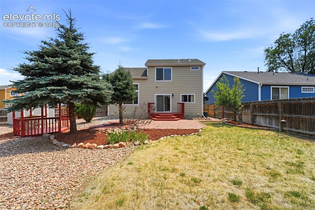 Image 36 of 48: Rear exterior featuring a brick paver patio, wood deck with red railing, an
