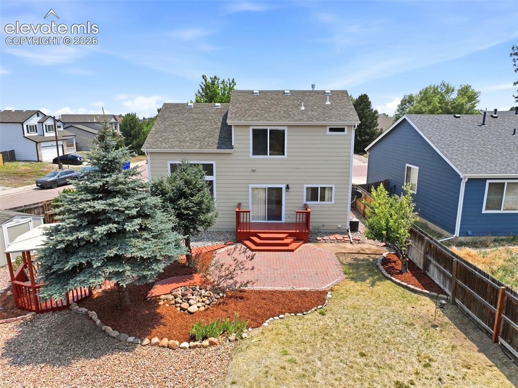 Image 42 of 48: Rear exterior featuring a red-stained deck, brick patio, and mature landsca