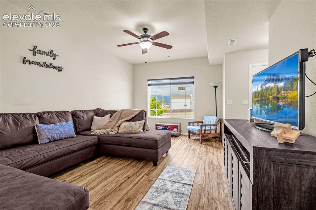Image 10 of 38: Spacious living area featuring wood-finish flooring, a ceiling fan with int