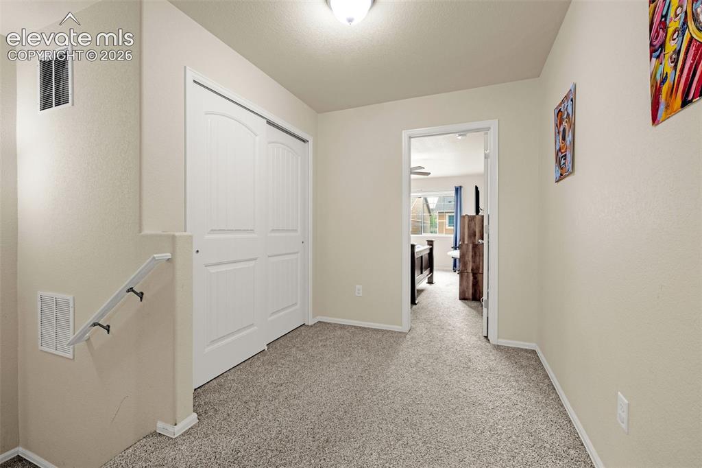 Image 25 of 38: Carpeted upstairs hallway featuring a white bi-fold closet, a white wall-mo