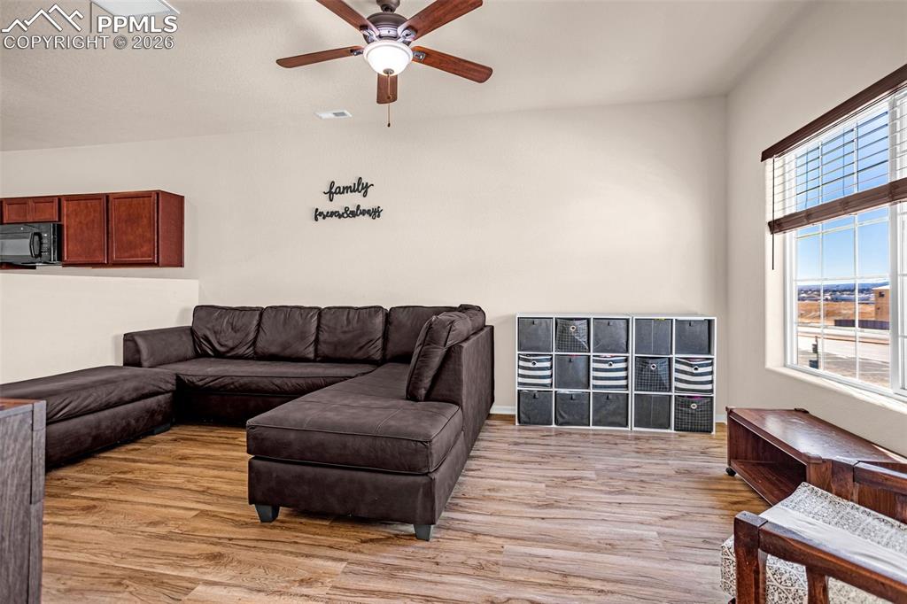 Image 5 of 30: Living area with light wood finished floors and ceiling fan
