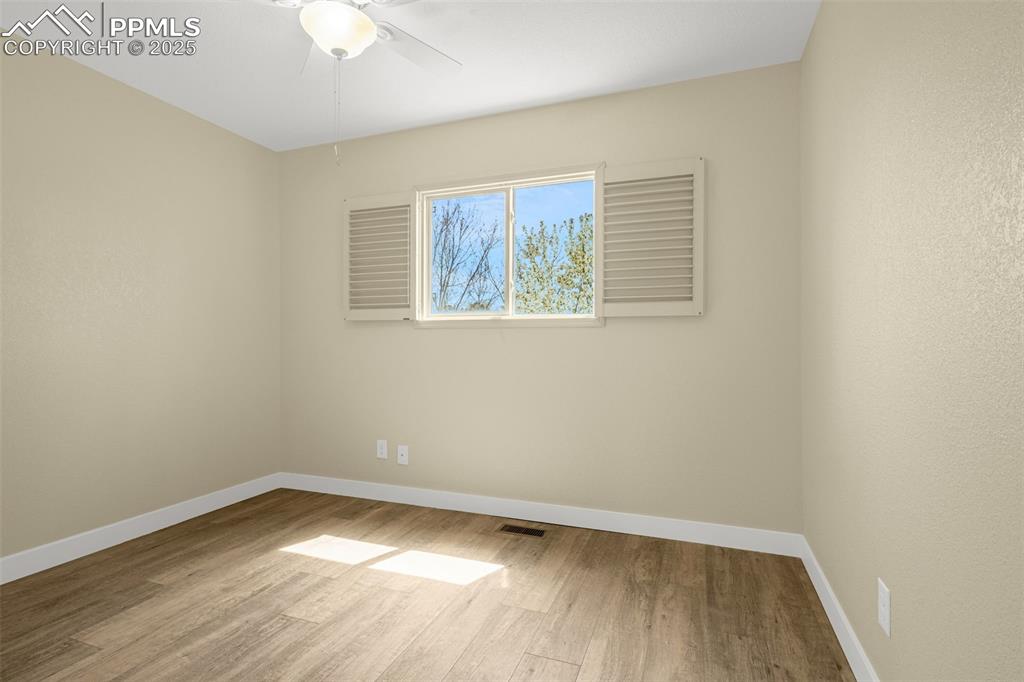 Image 11 of 36: Empty room with wood finished floors, ceiling fan, visible vents, and baseb