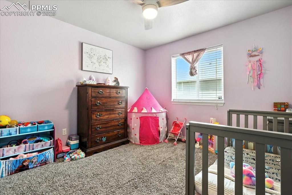 Image 15 of 31: Bedroom with carpet flooring, a ceiling fan, and a crib