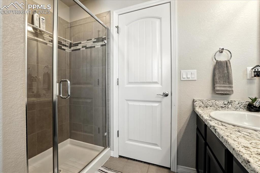 Image 18 of 31: Full bath with a textured wall, vanity, a stall shower, and light tile patt