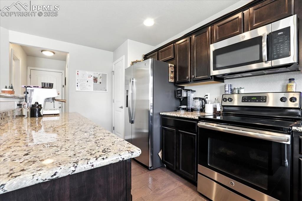 Image 24 of 31: Kitchen featuring stainless steel appliances, dark brown cabinets, light st